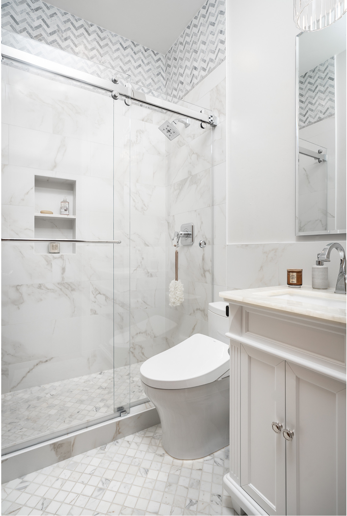 Bathroom remodel in Salmon Creek, WA featuring a marble-look tile shower with built-in niches, sliding glass door, and matching mosaic tile flooring.