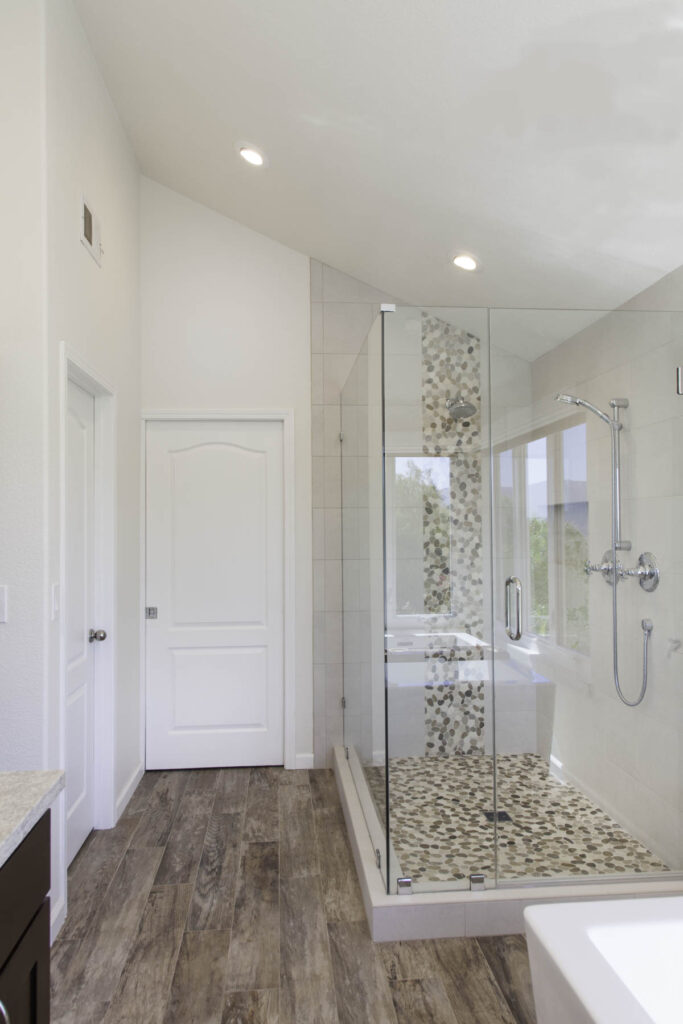 Modern bathroom remodel in Salmon Creek, WA with frameless glass shower, pebble-stone tile flooring, and chrome fixtures.