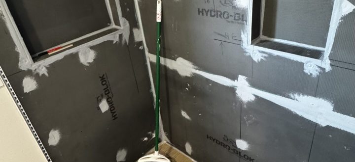 A bathroom in the early stages of renovation, featuring waterproofing materials like Hydro-Blok and marked measurements on the walls.