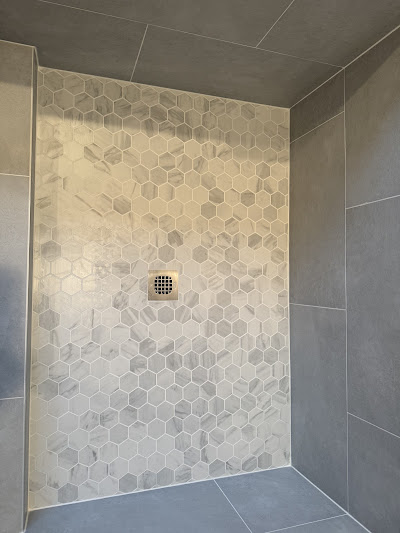 Stylish bathroom shower featuring hexagonal tiles with a subtle marbling effect on the floor and walls, paired with sleek, gray wall tiles for a modern aesthetic.