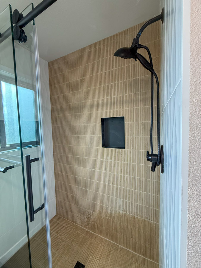 A modern shower enclosure with beige vertical subway tiles, black fixtures, and a minimalist design.