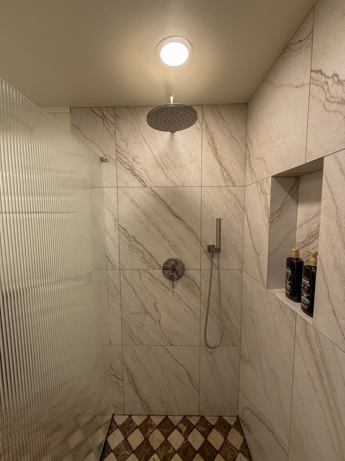 A sleek shower area featuring marble tiles, a rainfall showerhead, and recessed niches for storage, complemented by a checkered tile floor.