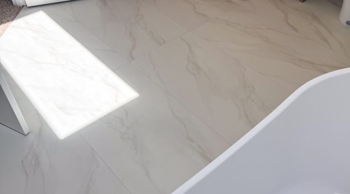 A luxurious freestanding bathtub with a polished gold drain, set on a marble floor in a modern bathroom.