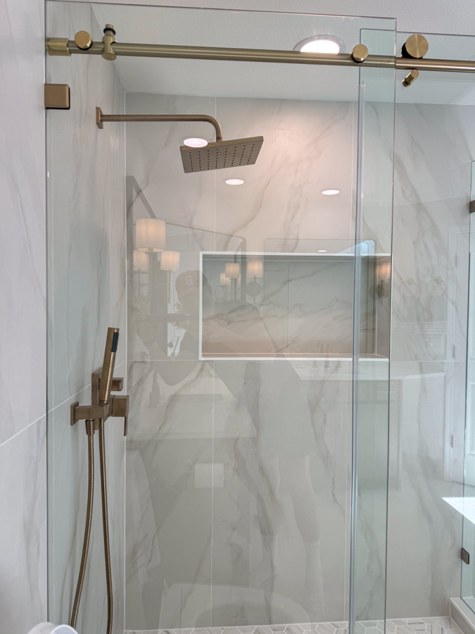 A sleek glass shower enclosure featuring gold fixtures, a rainfall showerhead, and marble tiles.