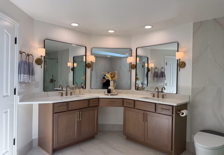 A luxurious bathroom with dual vanities, marble tiles, warm lighting from wall sconces, and a large mirror.