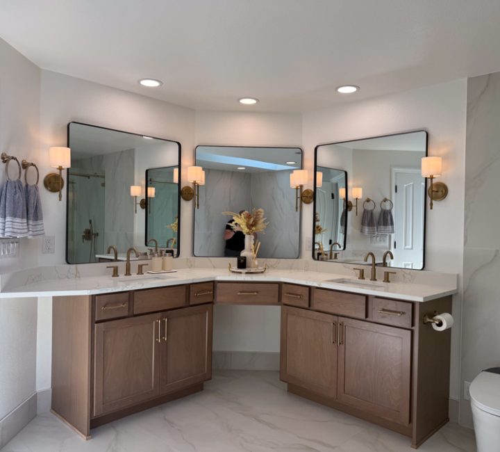 A luxurious bathroom with dual vanities, marble tiles, warm lighting from wall sconces, and a large mirror.