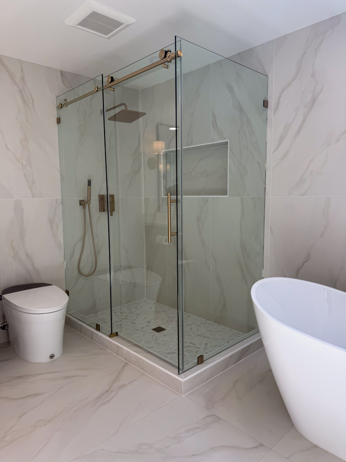 A sophisticated walk-in shower with white marble walls, a pebble tile floor, and gold accents.