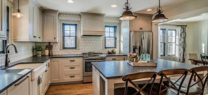 Classic kitchen interior with off-white cabinetry, subway tile backsplash, and a hardwood floor, featuring a central island with granite countertops.