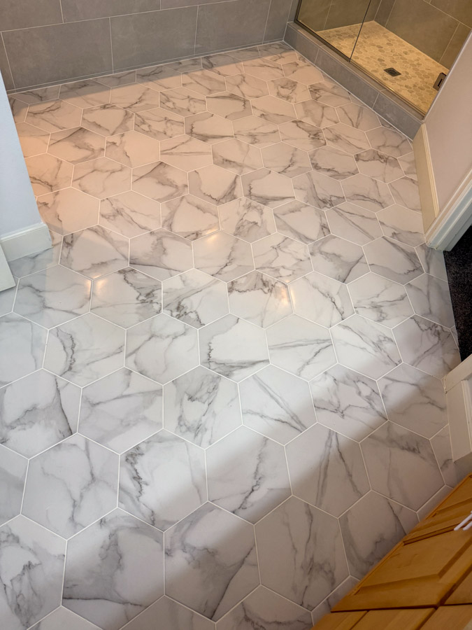 A bathroom floor covered in white hexagonal marble tiles with gray veining, creating a stylish and contemporary design.