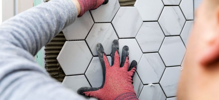 A tiler meticulously applying white ceramic tiles to a bathroom wall, demonstrating professional skill in ensuring uniform spacing and alignment.