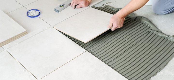A professional installer laying large, square floor tiles in a home, using tools to ensure level and correct spacing between the tiles.