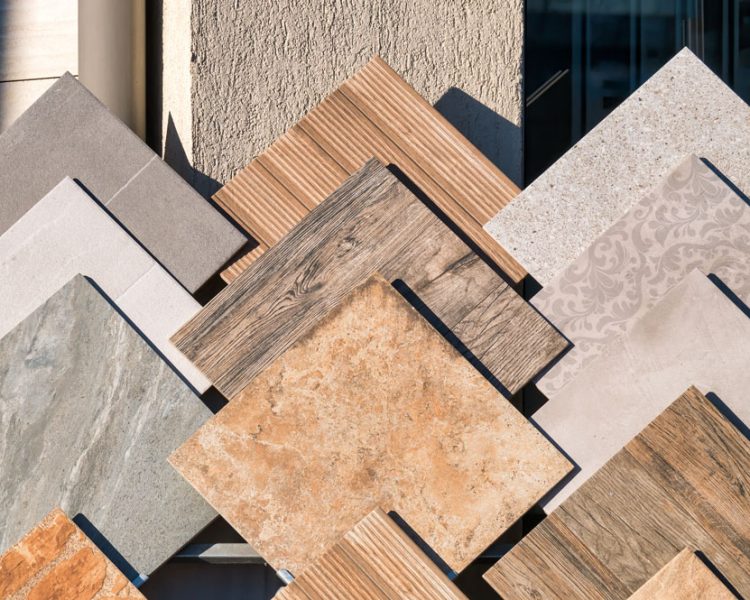 Variety of floor tile samples in different materials and colors, displayed on a sunlit surface, showcasing potential options for home improvement.