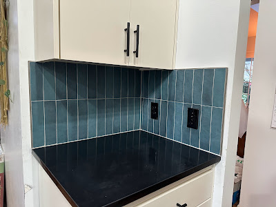 Modern kitchen corner showcasing teal subway tile backsplash that provides a vibrant contrast against the cream-colored cabinetry and black countertops.