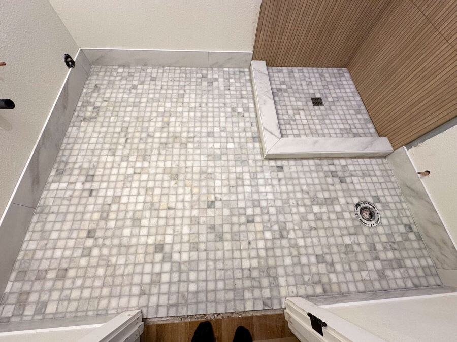 A luxurious walk-in shower with a combination of white marble tiles and a mosaic tile floor, offering a spa-like atmosphere.
