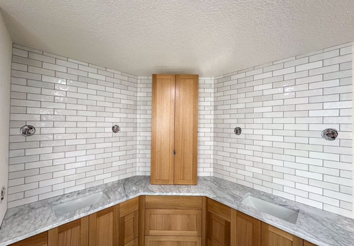 A contemporary bathroom featuring dual sinks, wooden cabinets, a white marble countertop, and a subway tile backsplash.