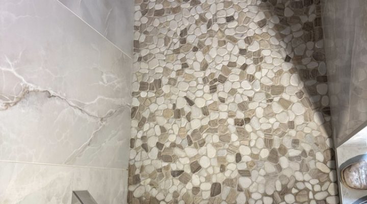 A shower area with a textured pebble mosaic tile wall, adding a tactile and visually appealing element to the design.