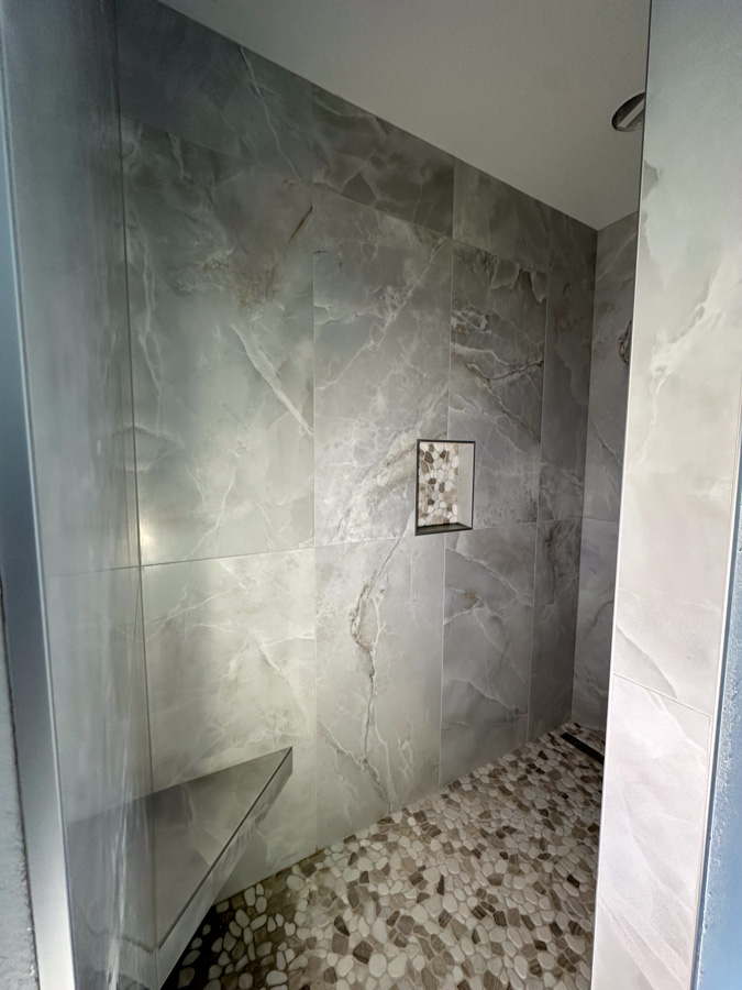 A contemporary bathroom featuring marble tiles on the walls and a glass partition, creating a sleek and elegant look.