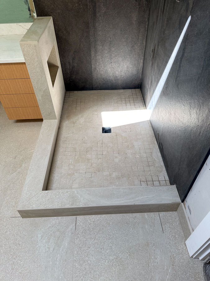 A contemporary bathroom setup with a built-in vanity, light-colored hexagonal floor tiles, and a minimalist design.