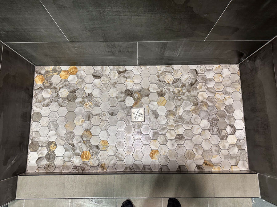 A modern walk-in shower area featuring hexagonal mosaic floor tiles with earthy tones and a sleek, clean design.