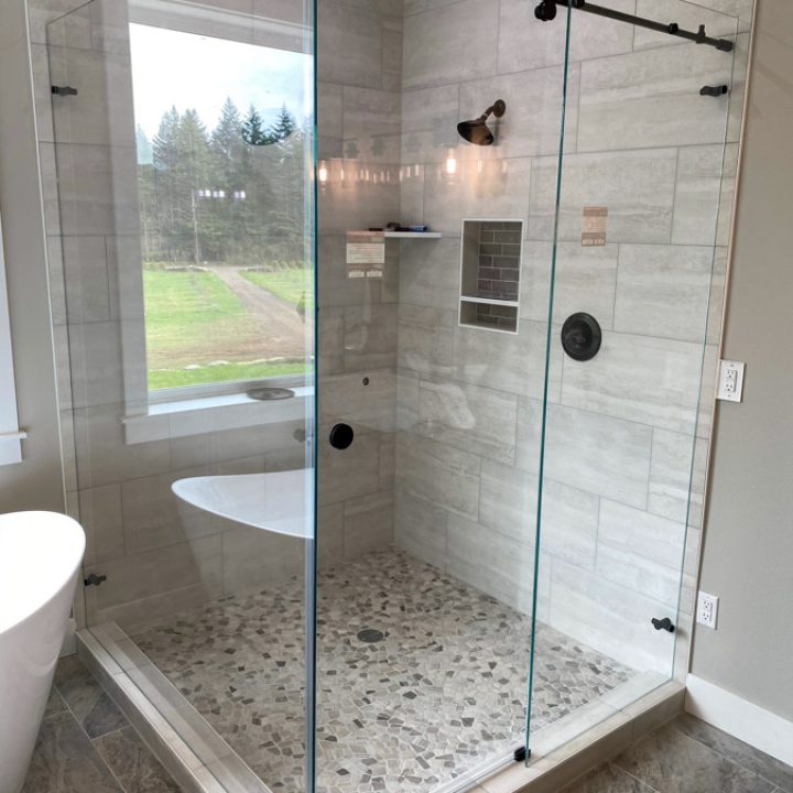 A stylish bathroom with a sliding glass shower door, offering a view of the outdoors through large windows.