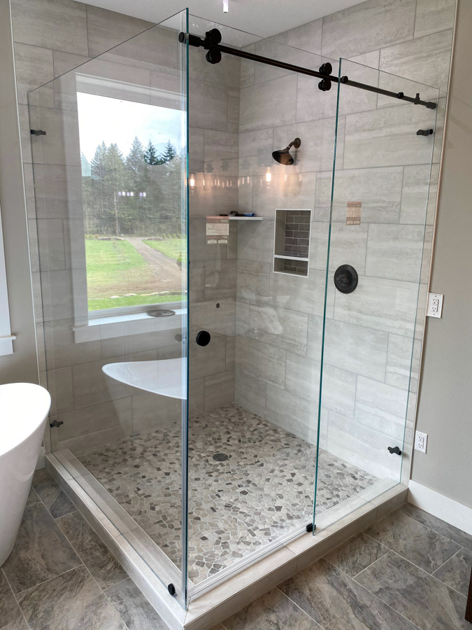 A stylish bathroom with a sliding glass shower door, offering a view of the outdoors through large windows.