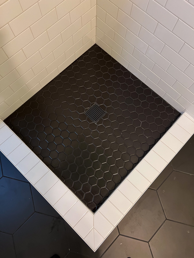 A bold design featuring a black hexagonal tile shower floor, contrasted by white trim and subway tiles.