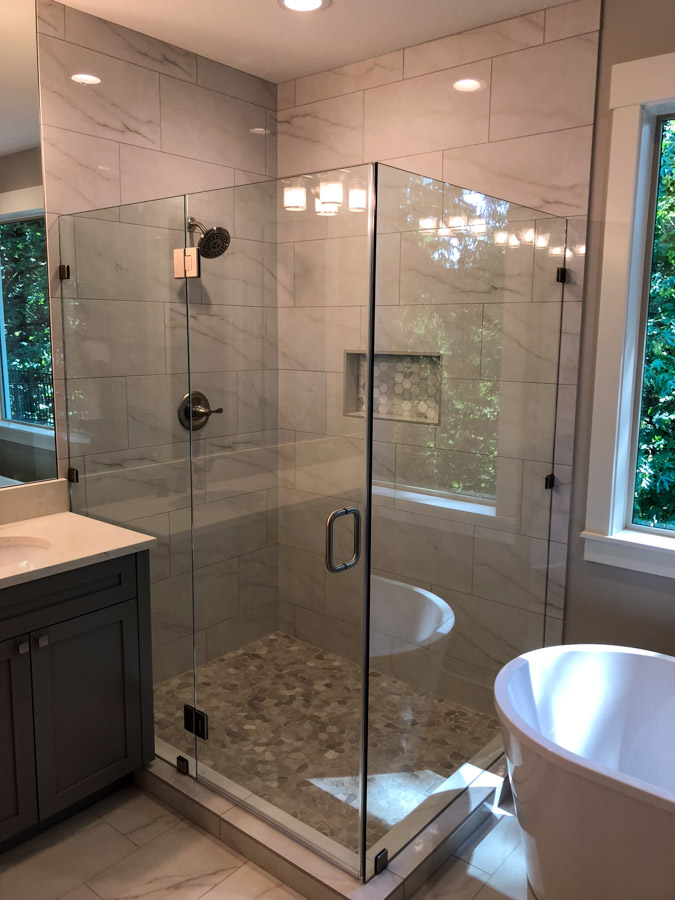 A contemporary bathroom featuring a frameless glass shower enclosure, a freestanding bathtub, and marble tiles.